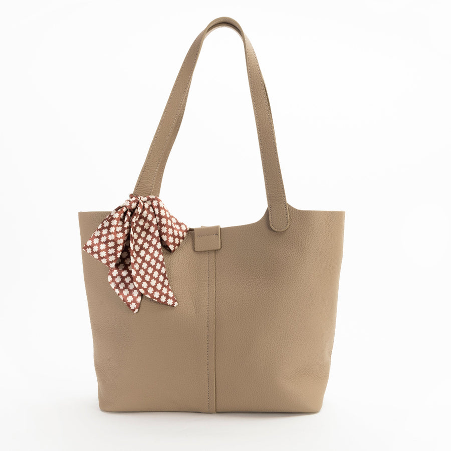 A beige leather tote bag with a detachable scarf in a zippered compartment, displayed against a plain background.